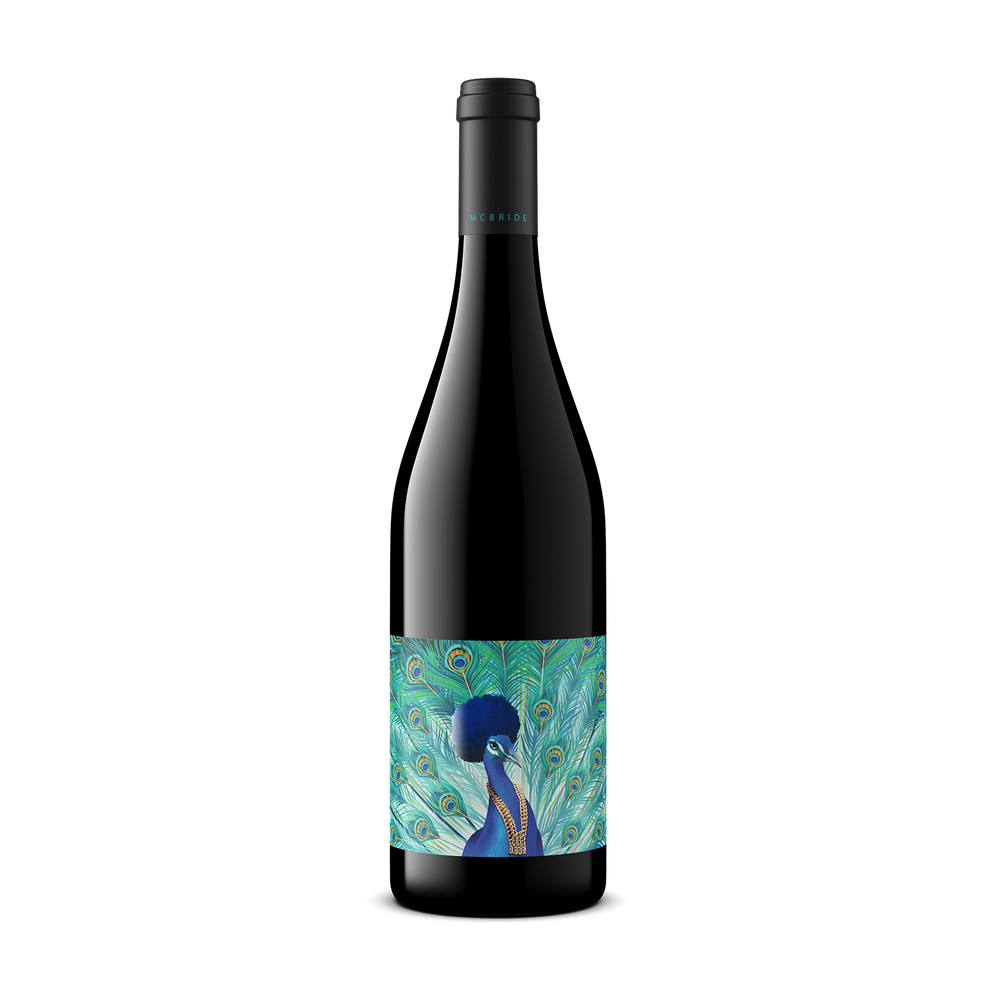 A dark glass wine bottle with a black capsule and a colorful label featuring a blue peacock with a teal peacock feather background, centered on a white background.