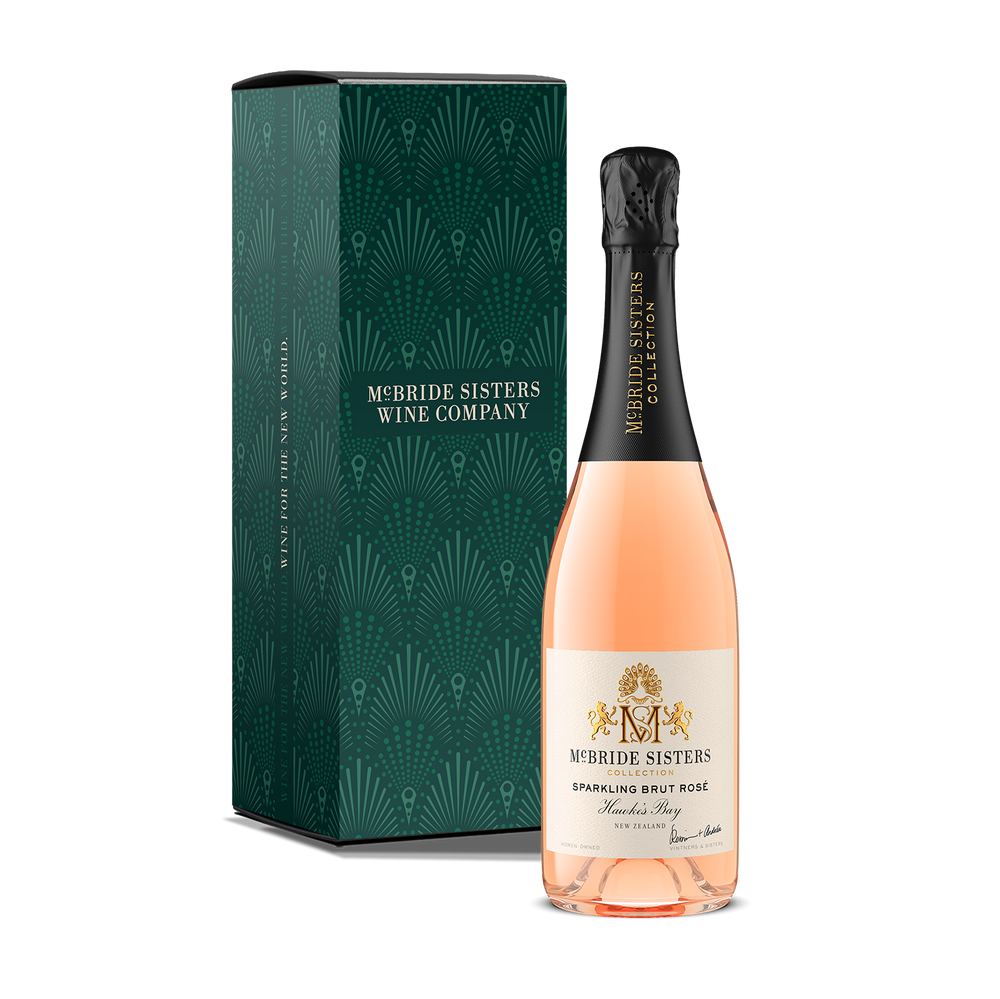 A bottle of McBride Sisters Wine Company sparkling brut rosé with a black capsule and pale pink liquid, shown in front of a dark green patterned gift box on a white background.