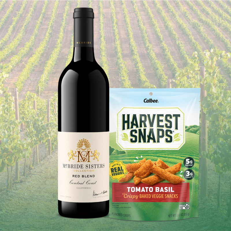 Mcbride Sisters Red Blend wine bottle next to a bag of Harvest Snaps Tomato Basil flavor. 